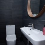 Black tiled private toilet with a small hand sink